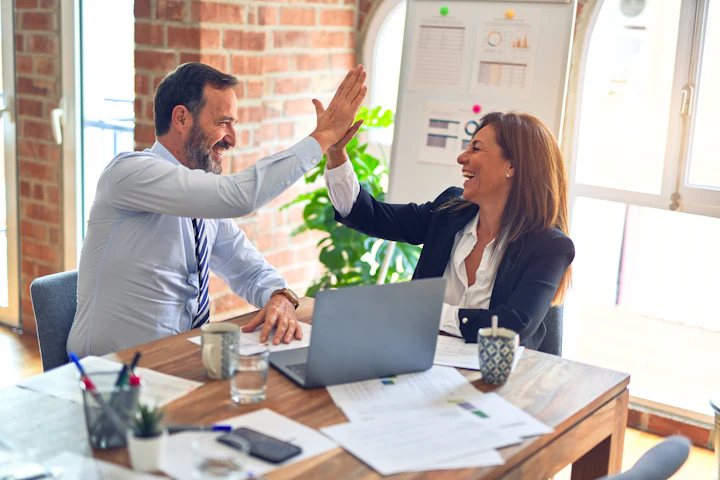 Two coworkers high-fiving across a desk